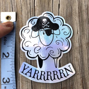 May include: Holographic sticker featuring a sheep wearing a pirate hat with a skull and crossbones. The sheep has an eye patch and the word "YARRRRRN" is written below. The sticker is approximately 2.5 inches tall.