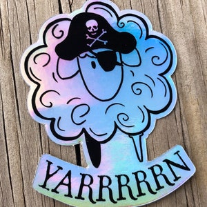 May include: Holographic sticker featuring a sheep with a pirate hat and eye patch. The sheep has a fluffy, cloud-like appearance with the word "YARRRRRN" in a banner below. The sticker has a pearlescent, iridescent finish.