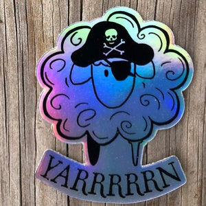 May include: Holographic sticker featuring a sheep wearing a pirate hat and eye patch. The sheep has a fluffy, cloud-like appearance with a blue and purple gradient. The word "YARRRRRN" is written below the sheep in a curved banner.