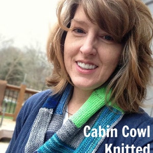 May include: A knitted cowl in shades of blue, green, gray, and red. The cowl is worn around the neck. The text "Cabin Cowl Knitted PDF Pattern" is displayed in white text on the image.