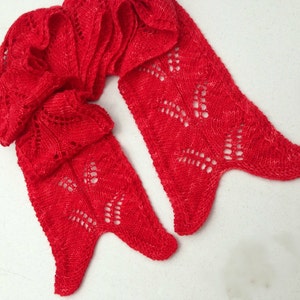 May include: A vibrant red knitted scarf with a delicate openwork design. The scarf is long and features a unique shape with pointed ends. The openwork pattern adds a touch of elegance and visual interest to the accessory.
