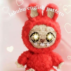 Può includere: Un giocattolo di peluche rosso con un cappuccio a forma di coniglio e occhi luminosi. Il giocattolo ha un viso beige con bocca e denti cuciti. Il testo "labubu english pattern" è scritto nella parte superiore dell'immagine.