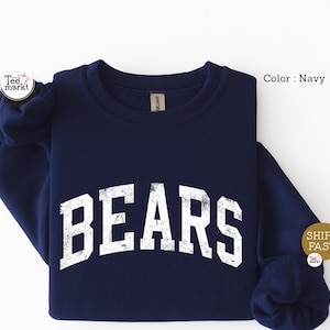 May include: A navy blue long-sleeve sweatshirt featuring the word BEARS printed in a large, white, distressed, arched varsity-style font across the chest. The garment has a crew neckline and long sleeves with ribbed cuffs, presented in a solid color.