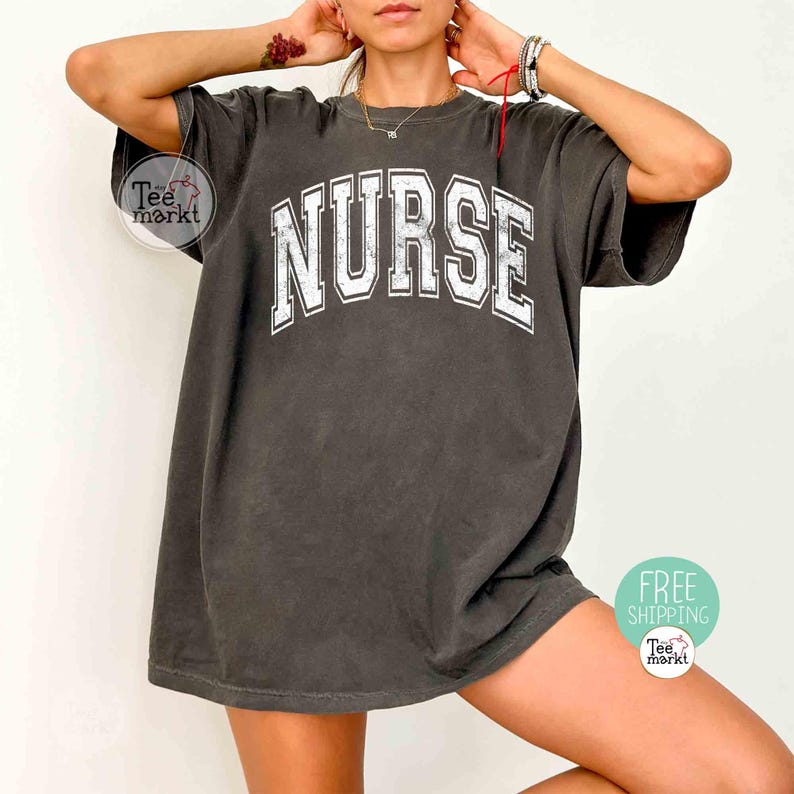 May include: Dark gray t-shirt with the word "NURSE" in large, white, block letters across the chest. The shirt has a vintage, slightly faded look. The tee is a relaxed fit.