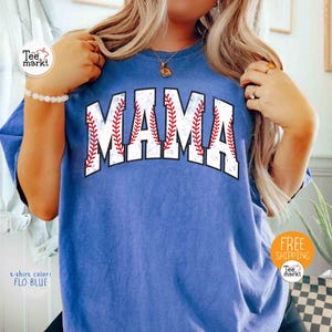 May include: A blue t-shirt featuring the word "MAMA" in large, white lettering with a baseball design. The letters have red stitching and a black outline. The text "t-shirt color: FLO BLUE" is visible on the shirt.