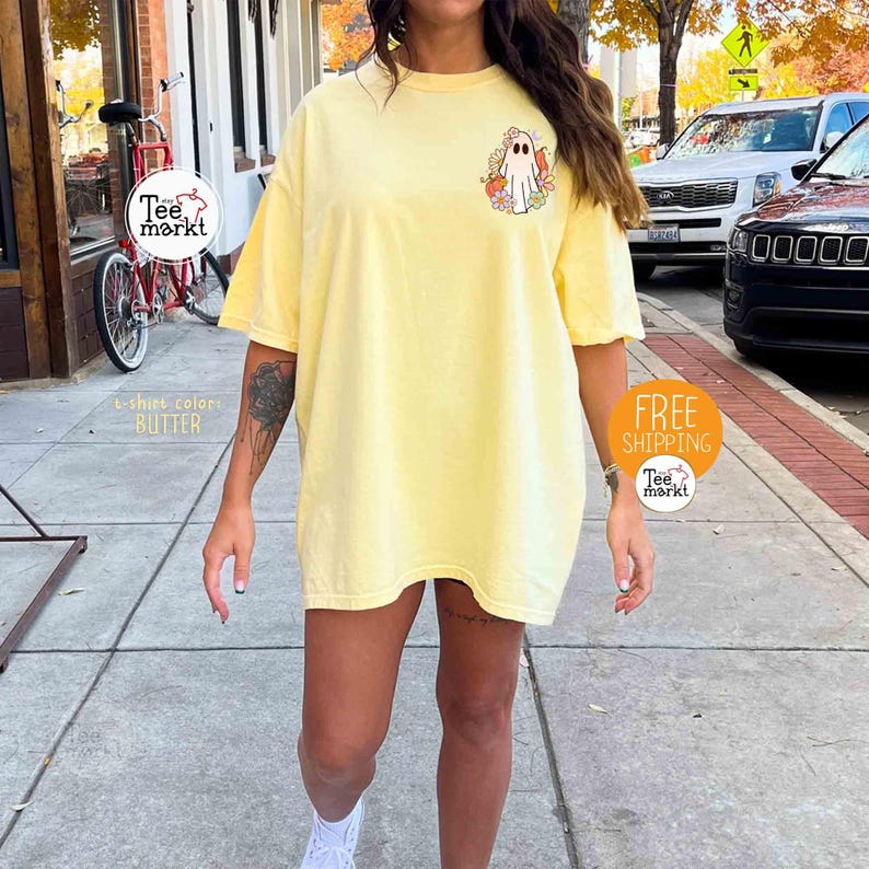 以下が含まれることがあります： ゴーストと花のグラフィックが特徴の、明るい黄色のTシャツ。 シャツは半袖でゆったりとしたフィット感です。 「Tee Markt」の文字が丸いステッカーに表示されています。 シャツの色は「バター」です。