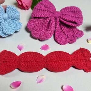 Puede incluir: Un lazo de ganchillo azul claro, un lazo de ganchillo magenta grande y una pieza de ganchillo roja larga con forma de caramelo. Un c&iacute;rculo naranja con el texto Crochet Pattern es visible. Los objetos est&aacute;n dispuestos con p&eacute;talos y hojas.