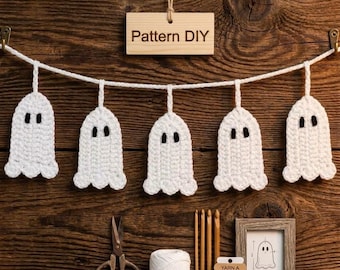 May include: A crochet ghost garland featuring five white ghosts with black eyes suspended from a white string. Below are metal scissors, a spool of white yarn, three wooden crochet hooks, and a small framed diagram labeled Pattern DIY.