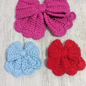 Puede incluir: Tres lazos de ganchillo hechos a mano en rosa brillante, azul claro y rojo. El lazo rosa grande est&aacute; colocado en la parte superior, mientras que los lazos m&aacute;s peque&ntilde;os azul claro y rojo est&aacute;n dispuestos uno al lado del otro debajo. Borde festoneado.