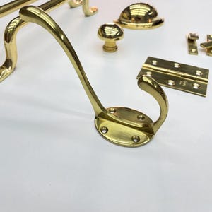A collection of polished brass hardware, including a coat hook, cabinet knobs،door handles, and hinges.The hardware is arranged on a white surface, showcasing the reflective quality of the brass.
