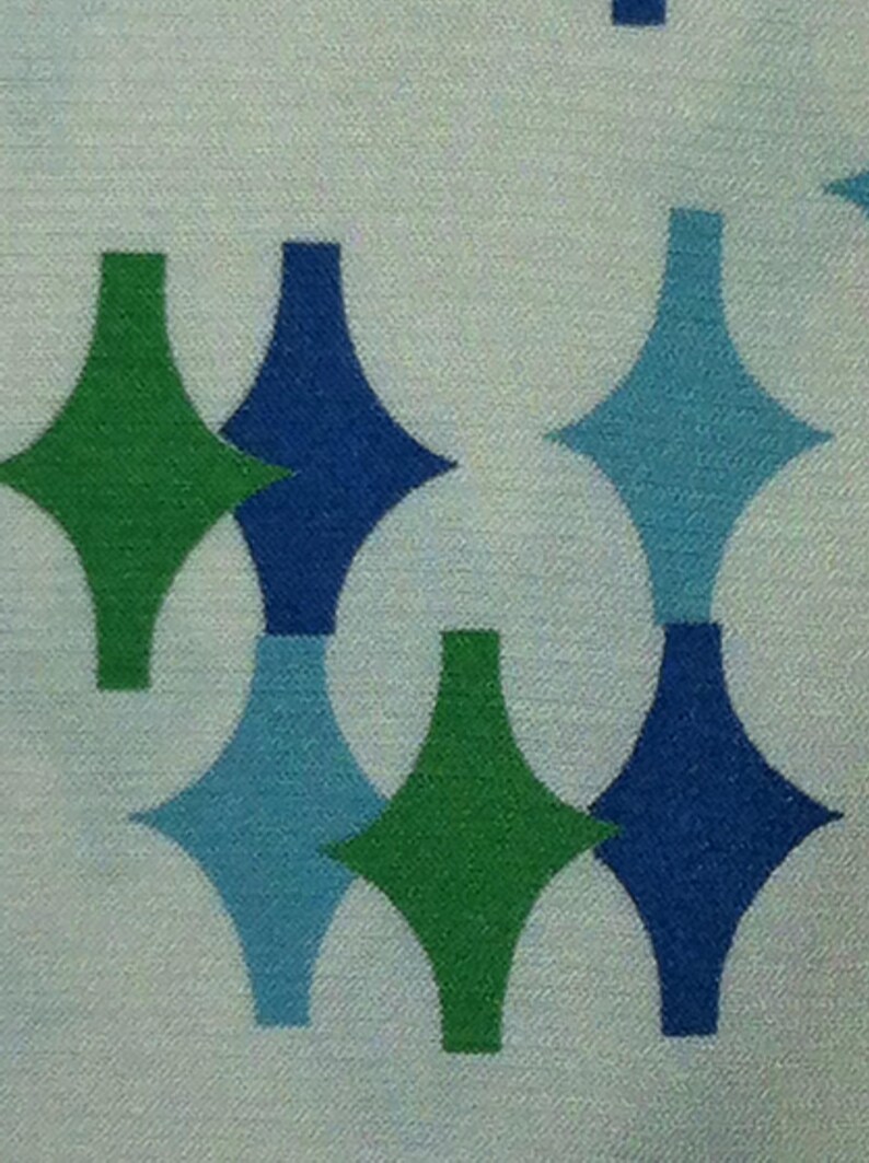 May include: A white fabric with a repeating pattern of green, blue, and light blue diamond shapes.