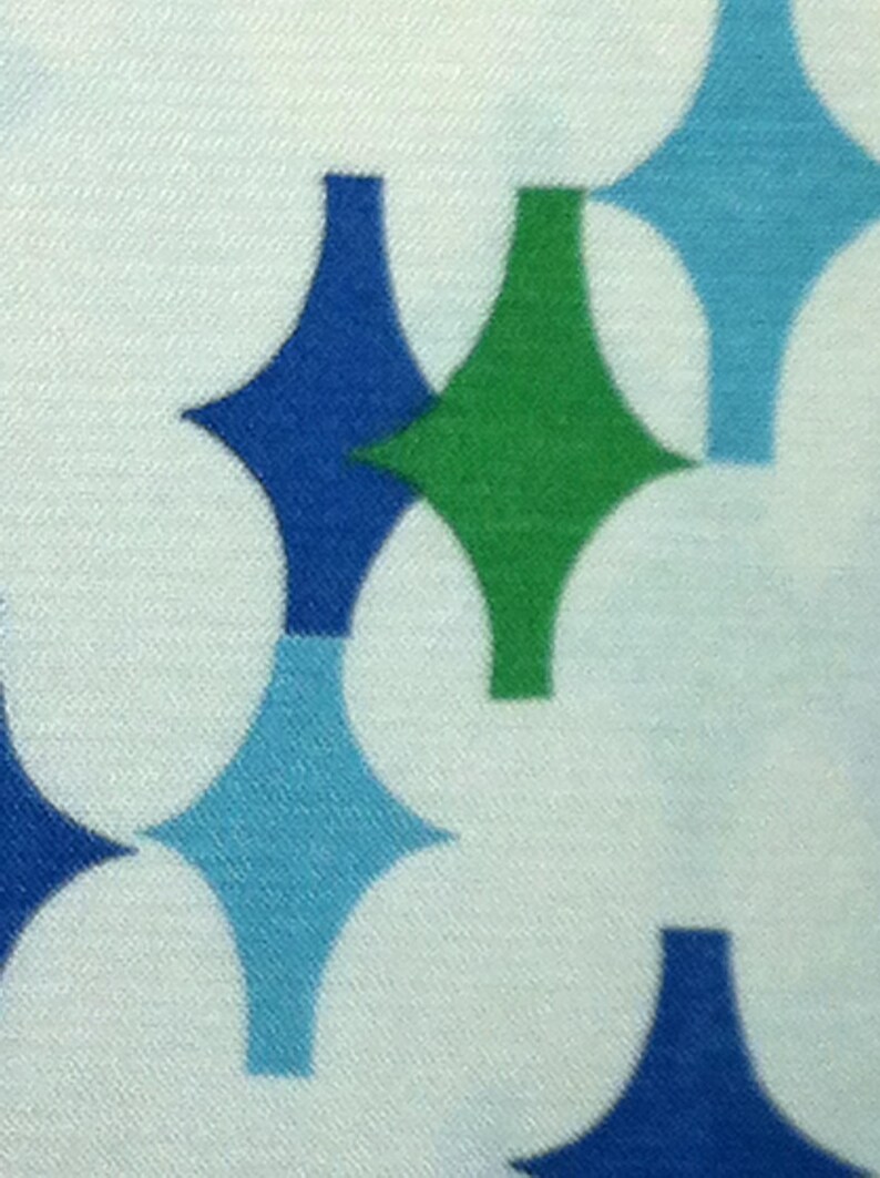May include: A white fabric with a repeating pattern of blue, green, and light blue diamond shapes.