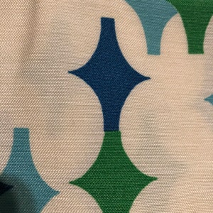 May include: A white fabric with a repeating pattern of green, blue, and dark blue diamond shapes.