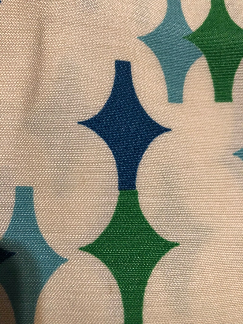 May include: A white fabric with a repeating pattern of green, blue, and dark blue diamond shapes.