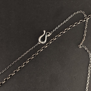 May include: A dark silver-toned metal chain necklace featuring a distinct hook-and-eye style clasp mechanism. The chain consists of interconnected circular links, and the clasp is marked with the number 925, indicating sterling silver composition.
