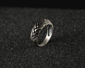 May include: A silver ring with a braided design. The ring is on a black textured surface.