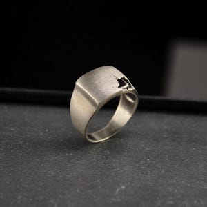 Puede incluir: Un anillo de plata con un diseño abstracto único. El anillo tiene una banda ancha y una superficie texturizada.