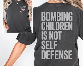 May include: Dark gray t-shirt with the text "BOMBING CHILDREN IS NOT SELF DEFENSE" in large, white letters on the back. The front of the shirt has a small image of a dove with the words "FREEDOM PALESTINE".