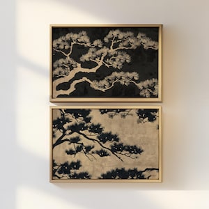 Puede incluir: Dos impresiones artísticas enmarcadas con ramas de pino estilizadas en negro y beige. La impresión superior tiene un fondo negro, la inferior uno beige. Ambas impresiones están en marcos de madera marrón claro.