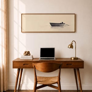 Puede incluir: Un escritorio de madera con un portátil, libros y una lámpara dorada. Una silla de madera con asiento tejido está frente al escritorio. Un cuadro enmarcado de un barco en el agua cuelga sobre el escritorio.