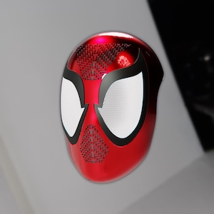 May include: A red and black Spider-Man mask with white eye lenses. The mask has a textured pattern on the top and around the mouth area. The eye lenses are white with a mesh pattern.
