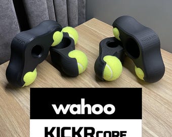 May include: Black plastic bike trainer stand with four yellow tennis balls attached. The stand has the text "Wahoo KICKR CORE" printed on it.