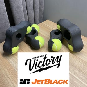 Könnte beinhalten: Zwei schwarze Tennisball-Trainingsgeräte mit gelben Tennisbällen. Die Geräte sind so konzipiert, dass sie die Griffkraft und die Hand-Augen-Koordination verbessern. Die Geräte sind mit "TUG-360" gekennzeichnet.