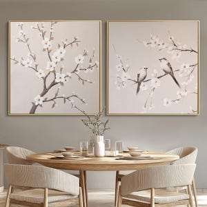 Puede incluir: Dos impresiones sobre lienzo enmarcadas con un fondo marrón claro. Las impresiones presentan un delicado diseño floral blanco con dos pájaros pequeños posados en las ramas. Las impresiones son perfectas para agregar un toque de naturaleza a cualquier habitación.