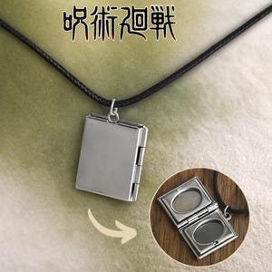 May include: A silver-colored rectangular pendant necklace with a black cord. The pendant opens to reveal two oval spaces. The Japanese text "Jujutsu Kaisen" is above the pendant. The pendant is shown closed and open.