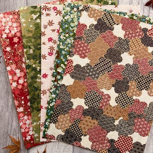 May include: A selection of patterned paper sheets in various colours and designs. The sheets feature floral, leaf, and geometric patterns in red, green, and brown hues. The papers are arranged on a wooden surface, with a few dried leaves scattered around.