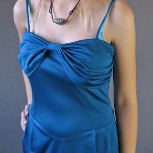 May include: A teal blue satin dress with a bow at the neckline. The dress has thin straps and a fitted bodice.