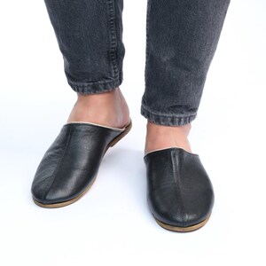 May include: A pair of black leather slippers with a white trim. The slippers have a rounded toe and a flat sole.