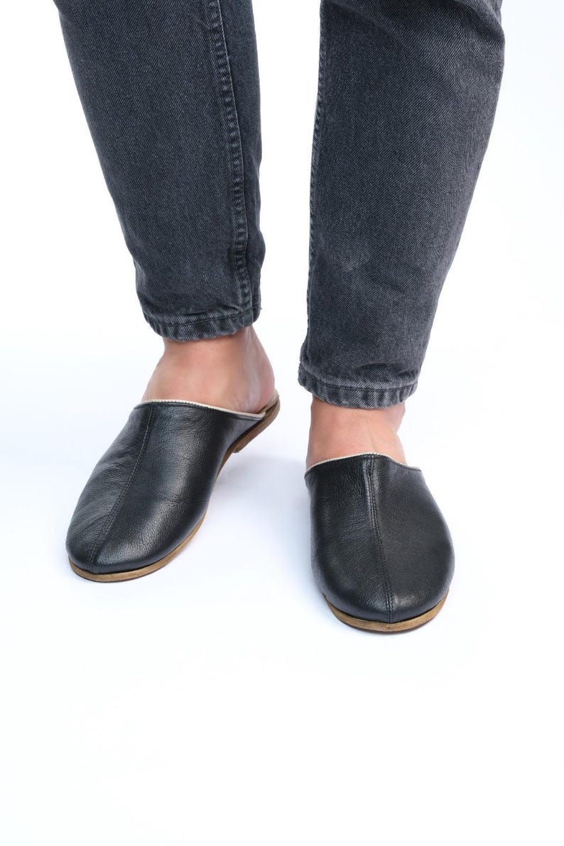 May include: A pair of black leather slippers with a white trim. The slippers have a rounded toe and a flat sole.