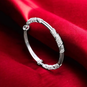 Puede incluir: Un brazalete de plata con un diseño floral. El brazalete está sobre un fondo rojo.