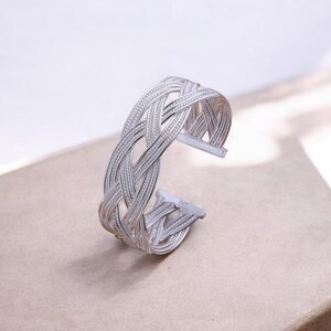 Puede incluir: Un brazalete de plata trenzado con un diseño tejido.
