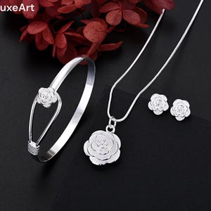 Peut inclure: Un ensemble de bijoux en argent composé d'un collier délicat avec un pendentif en forme de rose, d'un bracelet assorti avec un accent en forme de rose et d'une paire de boucles d'oreilles en forme de rose.