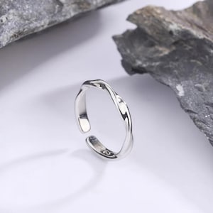 May include: A silver-coloured open ring with a twisted, undulating band design. The inner surface of the band features a small, stamped inscription that reads 925, indicating the metal composition. The ring has a polished, reflective finish.