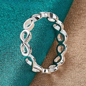 Puede incluir: Un anillo de plata con un diseño de símbolo de infinito. El anillo está hecho de metal y tiene un acabado pulido.