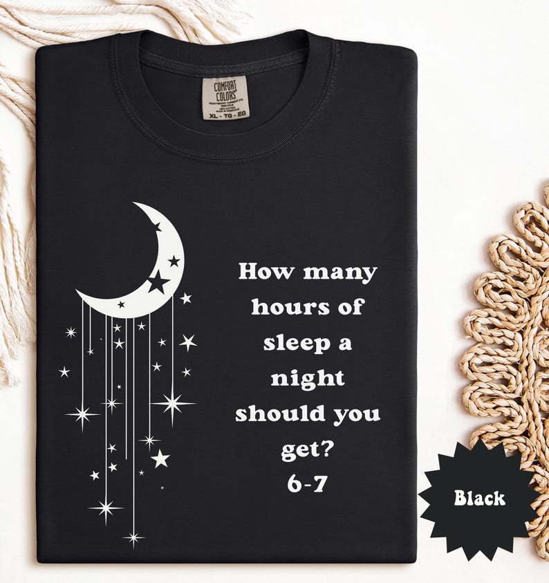 May include: Black t-shirt with a white crescent moon and stars design. The shirt features the text "How many hours of sleep a night should you get? 6-7". The shirt is a Comfort Colors brand.