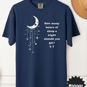 May include: Navy blue t-shirt with a white crescent moon and star design. The shirt features the text: "How many hours of sleep a night should you get? 6-7". The word "Midnight" is printed on a black starburst.
