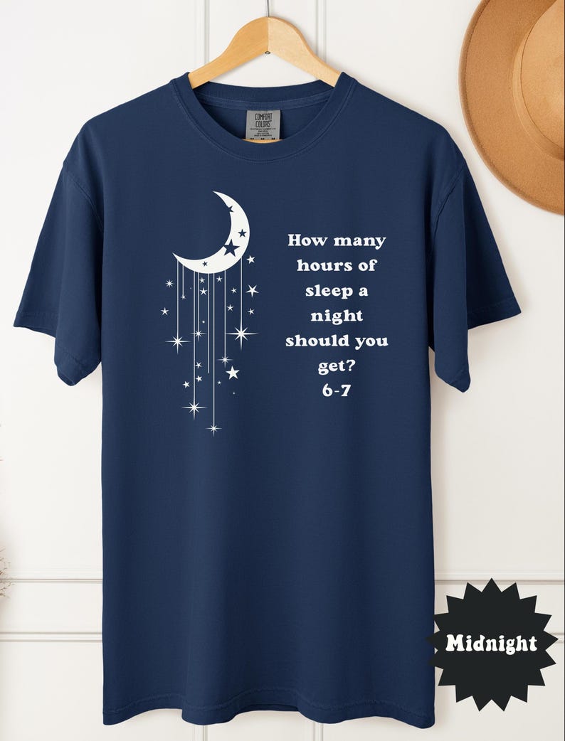 May include: Navy blue t-shirt with a white crescent moon and star design. The shirt features the text: "How many hours of sleep a night should you get? 6-7". The word "Midnight" is printed on a black starburst.