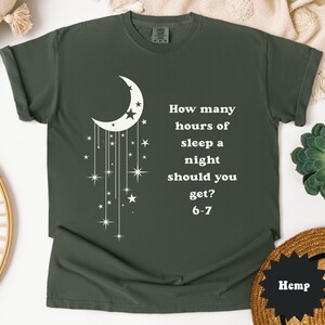 May include: Dark green t-shirt with a white crescent moon and star design. The shirt features the text "How many hours of sleep a night should you get? 6-7". The shirt is made of a soft material.