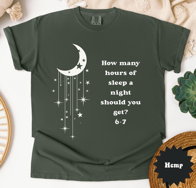 May include: Dark green t-shirt with a white crescent moon and star design. The shirt features the text "How many hours of sleep a night should you get? 6-7". The shirt is made of a soft material.