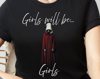 May include: Black t-shirt with the words "Girls will be... Girls" in white script. The shirt features a person in a red robe and white bonnet, a design inspired by a popular dystopian novel and TV series.