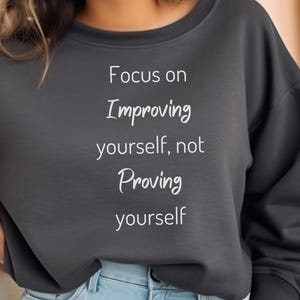 May include: A dark gray sweatshirt with the text "Focus on Improving yourself, not Proving yourself" printed in white.