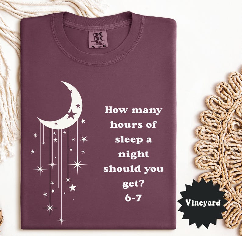 May include: A maroon Comfort Colors t-shirt with a white crescent moon and star design. The shirt features the text "How many hours of sleep a night should you get? 6-7". The tag reads "Vineyard".