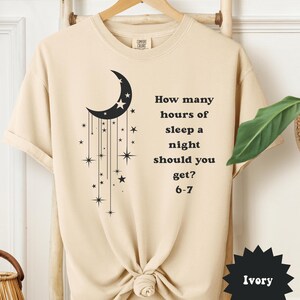 May include: Ivory-colored t-shirt with a black crescent moon and star design. Text on the shirt reads, "How many hours of sleep a night should you get? 6-7."
