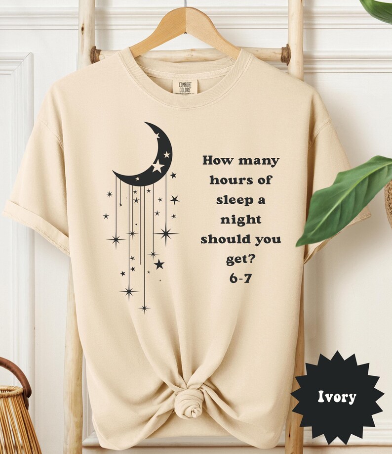 May include: Ivory-colored t-shirt with a black crescent moon and star design. Text on the shirt reads, "How many hours of sleep a night should you get? 6-7."