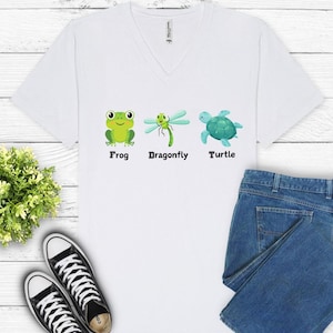 May include: White V-neck t-shirt with a green frog, dragonfly, and blue turtle graphic. The shirt has the words "Frog", "Dragonfly", and "Turtle" printed below each graphic.