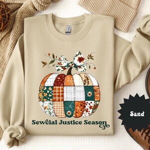 May include: Sand-colored sweatshirt featuring a patchwork pumpkin design with a bow and leaves. The pumpkin is composed of various fabric patterns in orange, green, and white. The text "Sewcial Justice Season" is printed below the pumpkin.